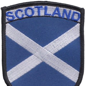 May include: A blue and white embroidered patch with the word "SCOTLAND" in blue lettering and a white saltire on a blue background. The patch has a black border.