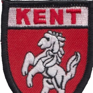 May include: An embroidered patch in red and white with a black border. The patch features the word "KENT" in red lettering on a white background. Below the word "KENT" is a white embroidered image of a white horse.