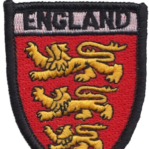 Puede incluir: Un parche bordado con fondo rojo y borde negro. El parche presenta tres leones dorados y la palabra "ENGLAND" en letras blancas.