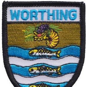 Può includere: Una toppa ricamata bianca con la parola "WORTHING" in lettere blu in alto. La toppa presenta uno sfondo marrone con un gambero giallo e arancione con un grappolo di uva viola. Tre linee ondulate blu con pesci gialli che nuotano al loro interno sono nella parte inferiore della toppa. La toppa è circondata da un bordo nero.