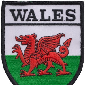 May include: An embroidered patch featuring a red dragon on a white and green background with the word "WALES" in black lettering at the top.