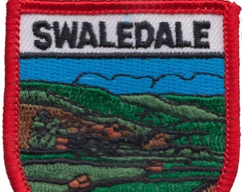 May include: A red, white, and blue embroidered patch with the word "SWALEDALE" in black lettering. The patch features a green and brown landscape with a blue sky.