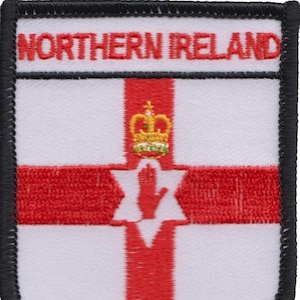 Puede incluir: Un parche bordado en blanco y negro con el texto "NORTHERN IRELAND" en la parte superior. El parche presenta la bandera de Irlanda del Norte, que incluye una cruz roja sobre un fondo blanco con una mano roja y una corona dorada.
