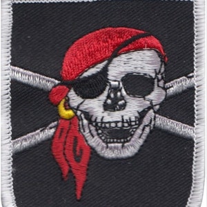 Op de afbeelding: Een zwarte geborduurde patch met een witte schedel die een rode bandana en een ooglap draagt. De schedel glimlacht en heeft gekruiste beenderen erachter.