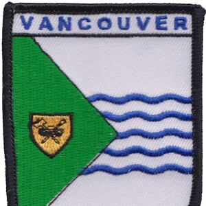 Peut inclure: Un écusson brodé vert et blanc avec le mot "VANCOUVER" en lettres bleues en haut. L'écusson présente un triangle vert avec un écu jaune contenant une image stylisée d'un gouvernail de navire et de deux haches croisées. La moitié inférieure de l'écusson est blanche avec trois lignes ondulées bleues.