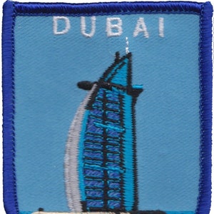 Op de afbeelding: Een blauwe en witte geborduurde patch met het woord "DUBAI" in witte letters en een blauwe en witte illustratie van het Burj Al Arab hotel.