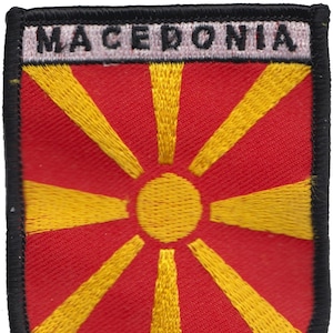 May include: Embroidered patch with the flag of Macedonia. The flag is red with a yellow sun in the center and eight yellow rays extending from the sun.