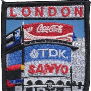 May include: Embroidered patch with a white background and red text that says "LONDON". The patch features a blue sky with a white and red Coca-Cola billboard, a blue and white TDK billboard, and a white and red Sanyo billboard. The bottom of the patch shows a white and gray depiction of a building with arches.