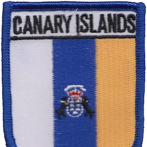 Puede incluir: Un parche bordado azul, blanco y amarillo con el texto "CANARY ISLANDS" en negro. El parche presenta un escudo de armas con una corona y dos leones.