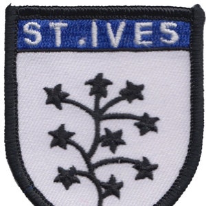 May include: A white embroidered patch with black stitching. The patch is shaped like a shield and features a black stylized plant with five-pointed stars. The text "ST. IVES" is embroidered in white on a blue banner at the top of the patch.