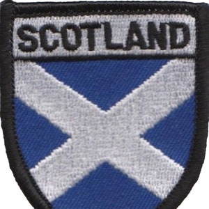 May include: A blue and white embroidered patch with the word "SCOTLAND" in black lettering. The patch features a white cross on a blue background.