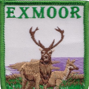 May include: Green embroidered patch with the word "EXMOOR" in white letters. The patch features a brown deer with large antlers and a smaller fawn standing in a field of green grass.