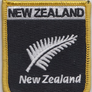 May include: A black and gold embroidered patch with a white fern and the text "New Zealand" in white.