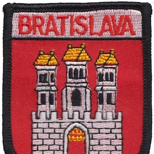 Könnte beinhalten: Gestickter Aufnäher mit dem Wappen von Bratislava, Slowakei. Der Aufnäher zeigt einen roten Hintergrund mit einem weißen Schloss mit drei Türmen und einem goldenen Tor. Der Text "BRATISLAVA" ist in Weiß auf einem weißen Banner über dem Schloss gestickt.