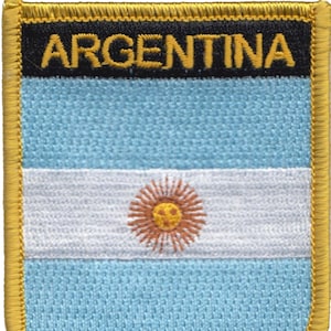 Op de afbeelding: Een blauwe en witte geborduurde patch met het woord "ARGENTINA" in gele letters op een zwarte achtergrond. De patch heeft een gouden rand.