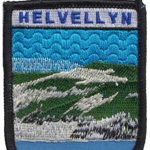 May include: A blue and green embroidered patch with the word "HELVELLYN" in white letters with a blue outline. The patch depicts a mountain scene with a blue sky and white clouds.