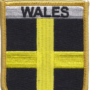 Peut inclure: Un écusson brodé or avec le mot "WALES" en lettres noires sur fond blanc. L'écusson présente une croix jaune sur fond noir.