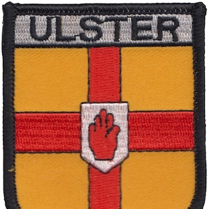 Puede incluir: Un parche bordado en rojo, blanco y dorado con la palabra "ULSTER" en letras blancas sobre un fondo gris. El parche presenta una mano roja con un contorno blanco sobre un fondo blanco.