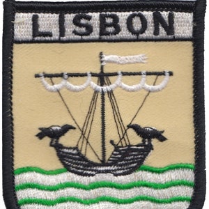 以下が含まれることがあります： 「LISBON」という文字が上部に刺繍された黒と白の刺繍パッチ。パッチには、白い帆と船首に2羽の黒い鳥がついた黒い船が、緑と白の波打つ海を航海している様子が描かれている。