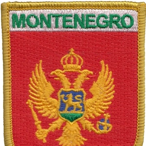 May include: A red embroidered patch with a gold border. The patch features the coat of arms of Montenegro, which includes a double-headed eagle with a shield and a crown. The text "MONTENEGRO" is embroidered in white with a green outline at the top of the patch.