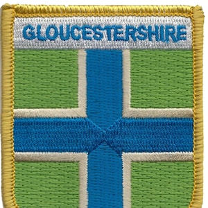 Könnte beinhalten: Ein gestickter Aufnäher mit der Flagge von Gloucestershire. Der Aufnäher ist grün, weiß und blau mit einem goldenen Rand und dem Text "GLOUCESTERSHIRE" in weiß.