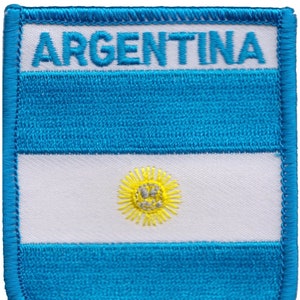 Può includere: Toppa ricamata con la bandiera argentina. La bandiera è blu e bianca con un sole giallo al centro. La parola "ARGENTINA" è ricamata in bianco nella parte superiore della toppa.