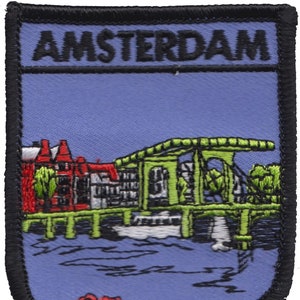 May include: Embroidered patch with a blue background and the word "AMSTERDAM" in black lettering. The patch depicts a green building with a red roof and a canal with water in blue and green hues.