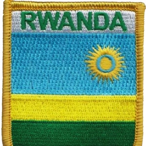 May include: A fabric patch with the word "RWANDA" in green letters on a white background. The Rwandan flag is depicted below, featuring a light blue field with a yellow sun in the center, a yellow stripe, and a green stripe.