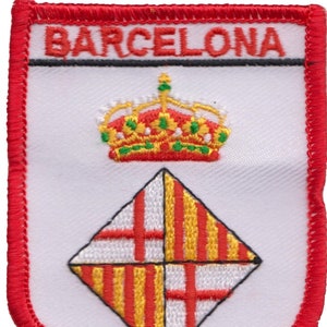 Puede incluir: Parche bordado en rojo, blanco y amarillo con la palabra "BARCELONA" en letras negras en la parte superior. Una corona roja con detalles verdes está sobre un diseño en forma de diamante con rayas rojas y amarillas.