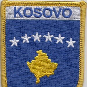 May include: Embroidered patch with a blue background, a yellow outline, and the word "KOSOVO" in white lettering. The patch features six white stars and a yellow outline of the country of Kosovo.