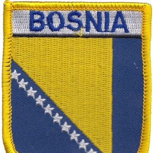 Può includere: Toppa ricamata raffigurante la bandiera della Bosnia ed Erzegovina. La toppa ha un bordo giallo e una forma a scudo. Il design della bandiera include un triangolo giallo, sfondo blu con stelle bianche e la scritta "BOSNIA" in blu.
