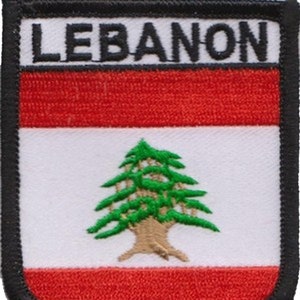 May include: A red, white, and green embroidered patch with the word "LEBANON" in black lettering at the top and the Lebanese flag in the center. The flag features a green cedar tree on a white background with two red horizontal stripes at the top and bottom.
