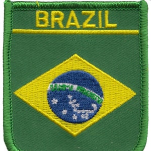 以下が含まれることがあります： 緑色の刺繍ワッペン。黄色の大文字で「BRAZIL」の文字が書かれています。その下に黄色と青色のブラジル国旗のデザインがあります。ワッペンの縁は緑色です。