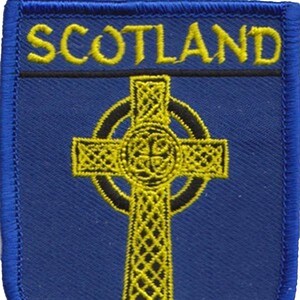 Könnte beinhalten: Ein blauer gestickter Aufnäher mit dem Wort "SCOTLAND" in gelben Buchstaben und einem gelben keltischen Kreuz mit schwarzem Umriss.