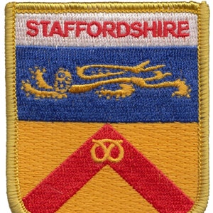 May include: A gold embroidered patch with the text "STAFFORDSHIRE" in red lettering. The patch features a blue background with a gold dragon and a yellow background with a red chevron and a gold knot.
