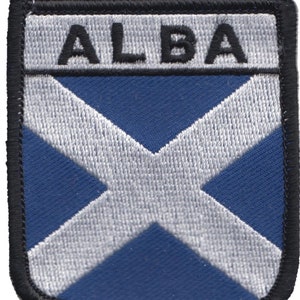 May include: A blue and white embroidered patch with the word "ALBA" in black lettering. The patch features a white cross on a blue background.