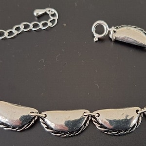 Op de afbeelding: Een zilveren armband met een ketting en een reeks verbonden halvemaanvormige schakels.