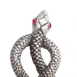 May include: A silver-colored snake-shaped decorative item with red eyes. The snake is coiled in an infinity symbol shape. The scales are detailed and textured. The background is white.