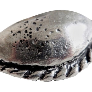 May include: A silver-coloured metal charm shaped like a pastry, with a detailed, textured surface.