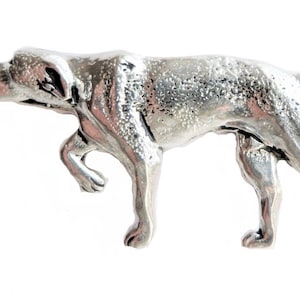 以下が含まれることがあります： 銀色のピューター製のポインティングドッグの置物。犬は4本足で立っており、頭は左を向いています。置物は、テクスチャのある表面で詳細に作られています。