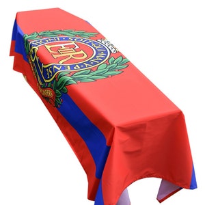 Puede incluir: Un mantel rectangular rojo con rayas azules y un diseño de escudo. El escudo presenta las letras "ER" y las palabras "HONI SOIT QUI MAL Y PENSE" en un patrón circular, con una corona de laurel.