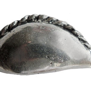 May include: A silver-coloured metal charm shaped like a pastry with a rope-like design around the edge.