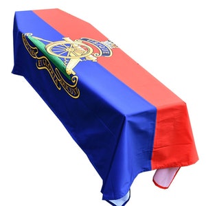 Puede incluir: Un mantel azul y rojo con un escudo dorado que presenta una rueda de cañón y las palabras "Ubique et Globla Ducunt".
