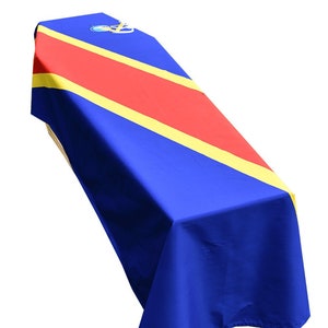 May include: A blue, red and yellow casket drape with a diagonal stripe pattern. The drape is made of fabric and has a gold emblem in the top left corner.