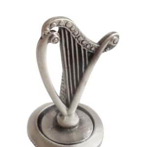May include: Silver bottle stopper shaped like a harp with a cork base.