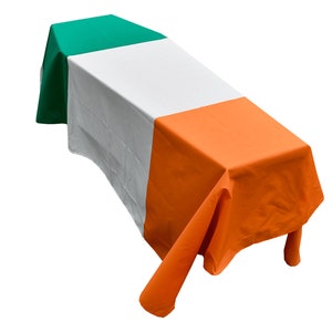 May include: A white tablecloth with green, white and orange stripes. The tablecloth is draped over a table and the edges are hanging down.