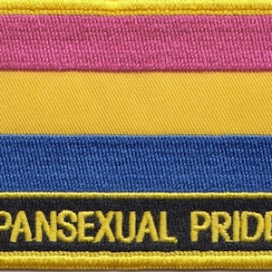 May include: A yellow, blue and pink pansexual pride flag patch with the text "PANSEXUAL PRIDE" in black.