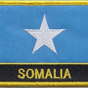 Może przedstawiać: Naszywka haftowana w kolorze niebieskim i białym z białą gwiazdą w środku i napisem "SOMALIA" w żółtych literach na czarnym tle.