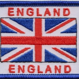 Może przedstawiać: Biała naszywka haftowana z czerwoną, białą i niebieską flagą Unii w środku. Słowa "LONDON ENGLAND" są wyszyte na niebiesko po lewej i prawej stronie flagi.