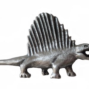 May include: A silver-coloured pewter pin of a dinosaur with a large, spiky fin on its back. The dinosaur is standing on all fours with its mouth open.
